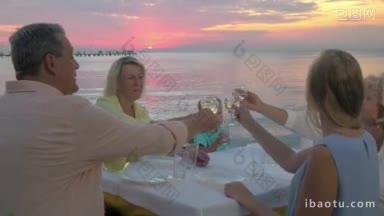 夕阳西下，一大家子人在海边的户外餐厅里，大人们摇着酒杯喝酒，孩子喝水